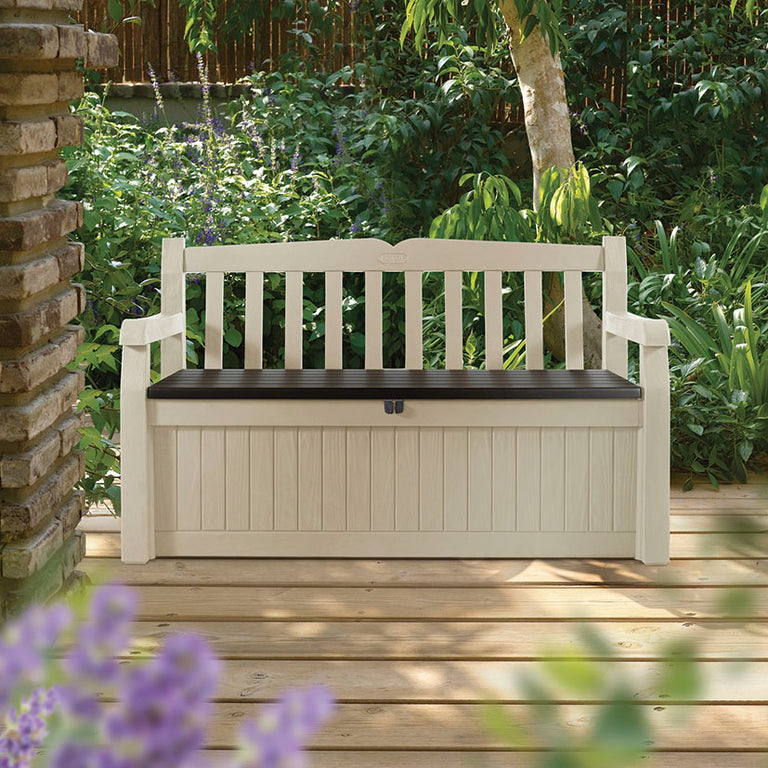 Banco de jardín Keter Edén cerrado ubicado en una terraza de madera con plantas de fondo, diseño imitación madera beige.