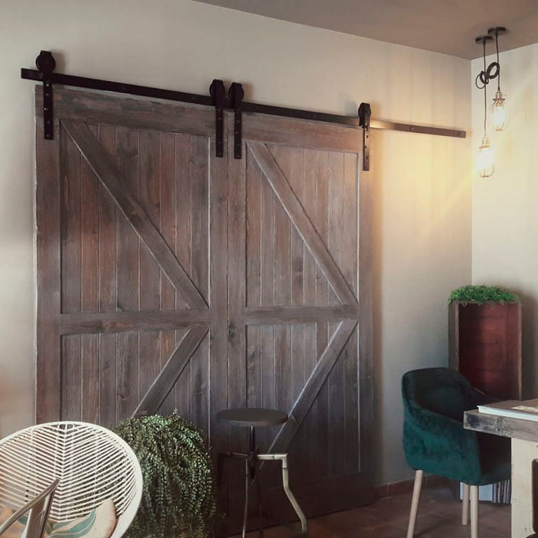 Puerta doble de madera rústica instalada con sistema de herrajes tipo granero Estebro en color negro.