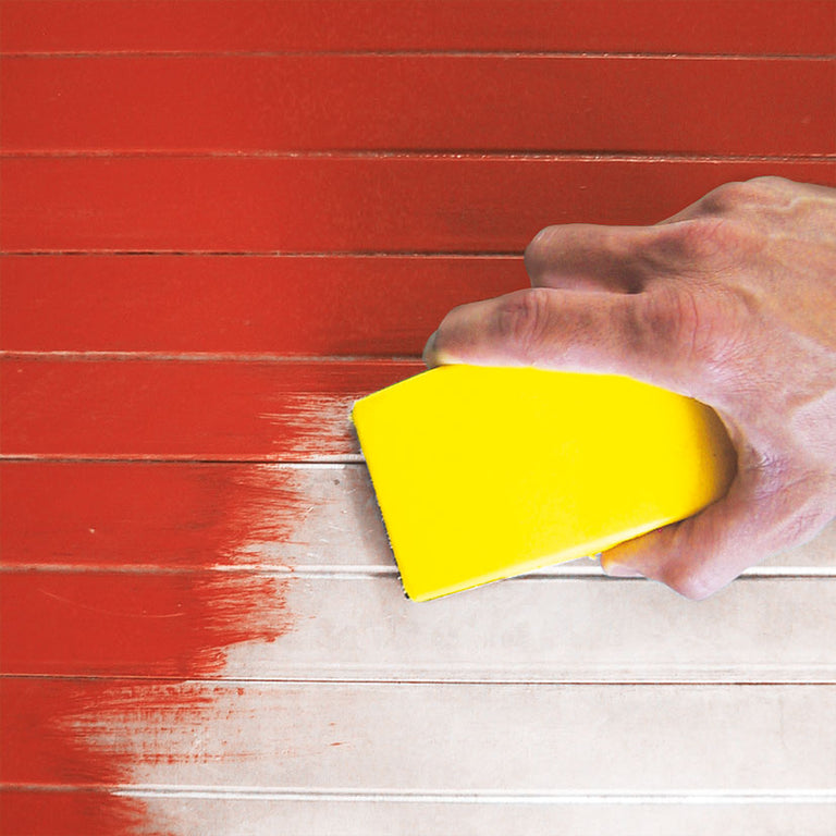 Lijado manual con taco amarillo sobre superficie de madera pintada de rojo