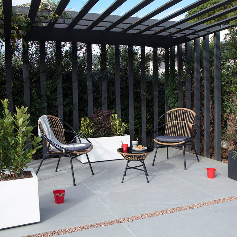 Sillones de exterior con estructura metálica negra y cojines grises situados bajo una pérgola de diseño.