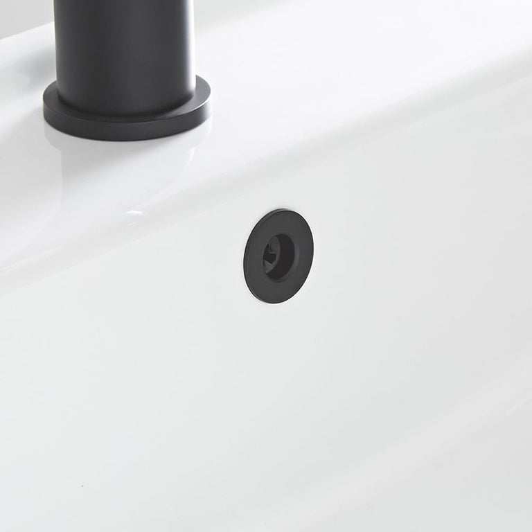 Detalle de embellecedor negro instalado en el orificio de rebosadero de un lavabo cerámico blanco