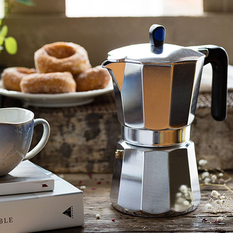 Cafetera Monix Induction Express en mesa de desayuno junto a tazas de café y dulces.