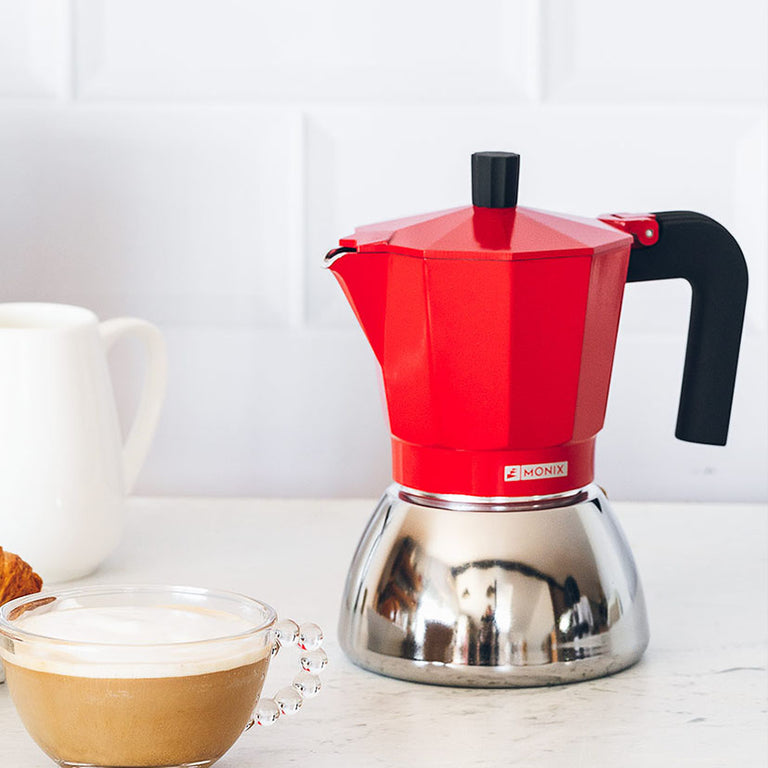 Cafetera Monix roja junto a taza de café en encimera blanca