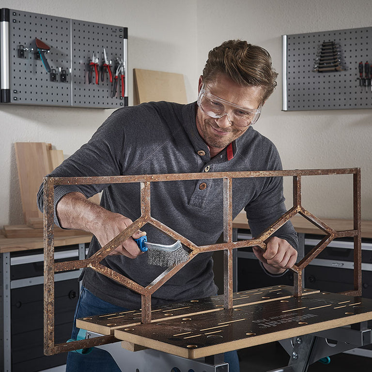 Uso de cepillo Wolfcraft para limpiar una estructura de hierro oxidada en un banco de trabajo de taller.