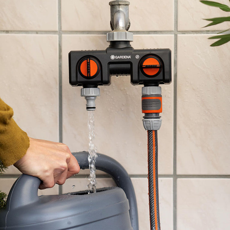 Distribuidor Gardena instalado en grifo exterior llenando una regadera y conectado a una manguera de riego.