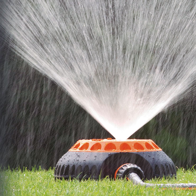 Aspersor Claber multifunción regando césped con chorro de agua fino y uniforme en abanico sobre jardín verde.