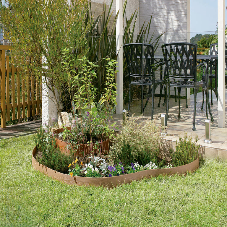 Aplicación de bordura flexible de composite delimitando un parterre con flores y plantas en un jardín.