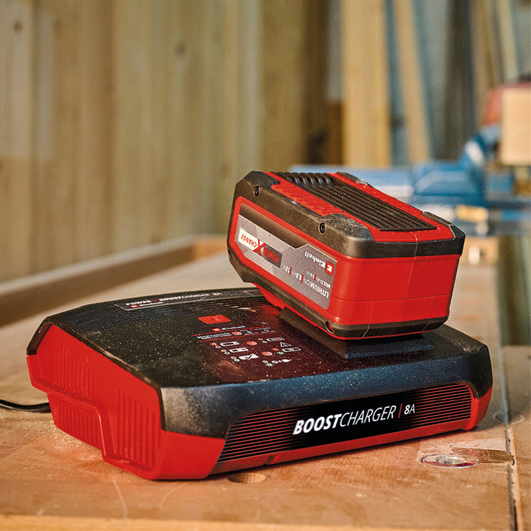 Batería Einhell Power X-Change de 18V conectada al cargador rápido de 8A en un banco de trabajo.