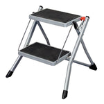 Taburete plegable de acero Habitex de 2 peldaños con plataformas antideslizantes negras y patas con tacos.