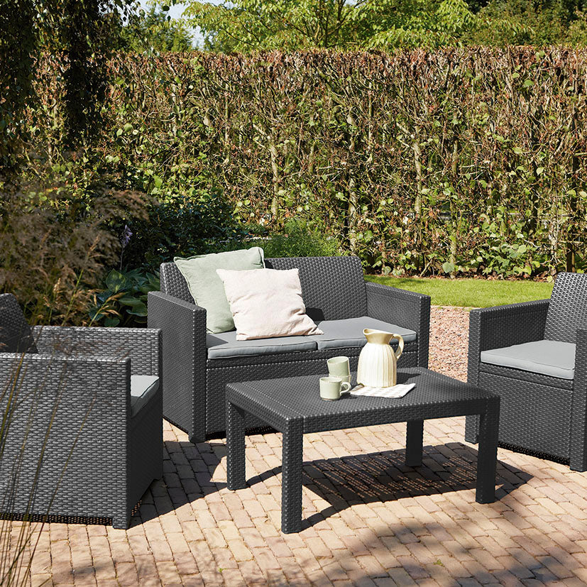 Set de muebles de exterior Keter Merano instalado en un patio con cojines grises y decoración de jardín.