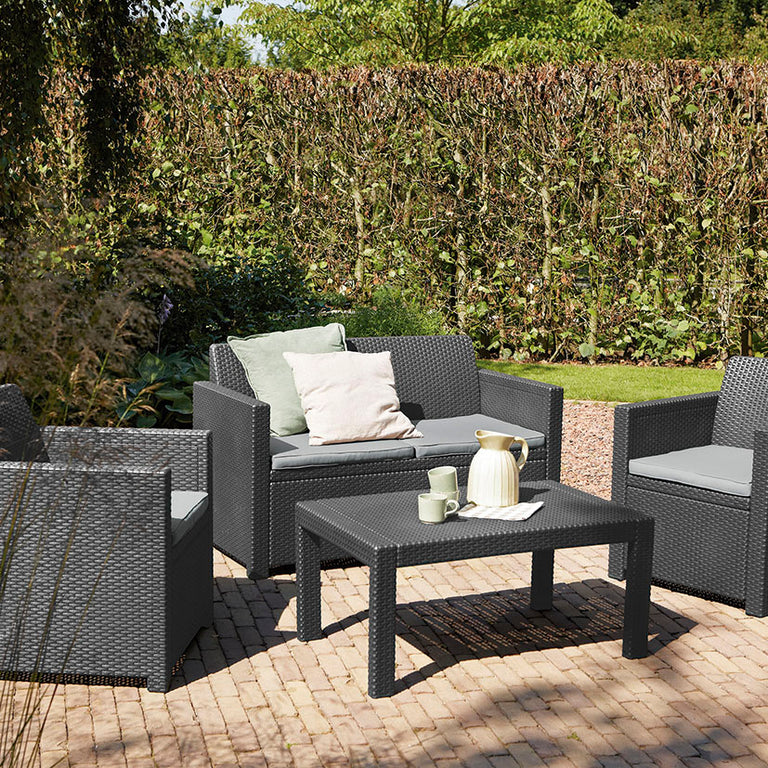 Set de muebles de exterior Keter Merano instalado en un patio con cojines grises y decoración de jardín.