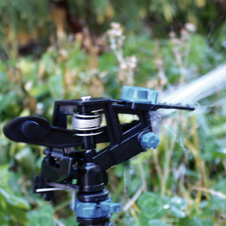 Primer plano del cabezal del aspersor de impacto en funcionamiento pulverizando agua en un jardín.