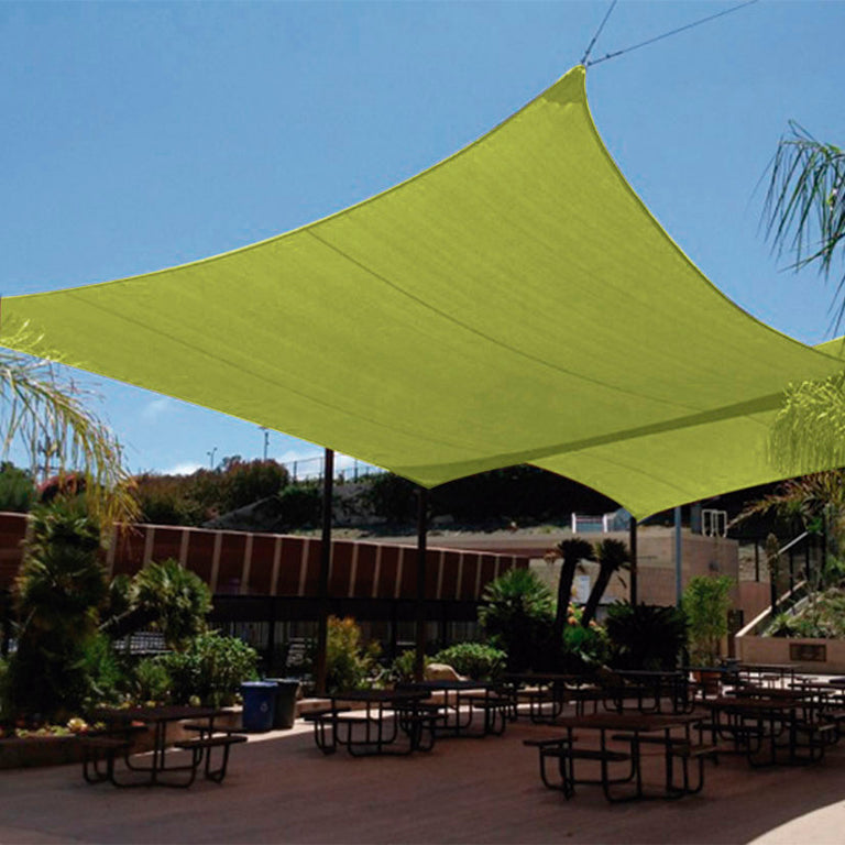Toldo vela cuadrado verde pistacho instalado sobre zona de comedor exterior con mesas y bancos.