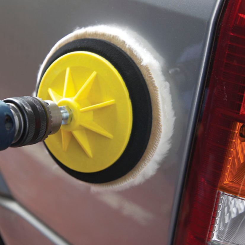Taladro eléctrico con plato autogrip y disco de lana puliendo la carrocería de un coche gris.