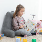 Niña sentada en el suelo sobre alfombra usando la almohada con apoyabrazos para leer un cuento