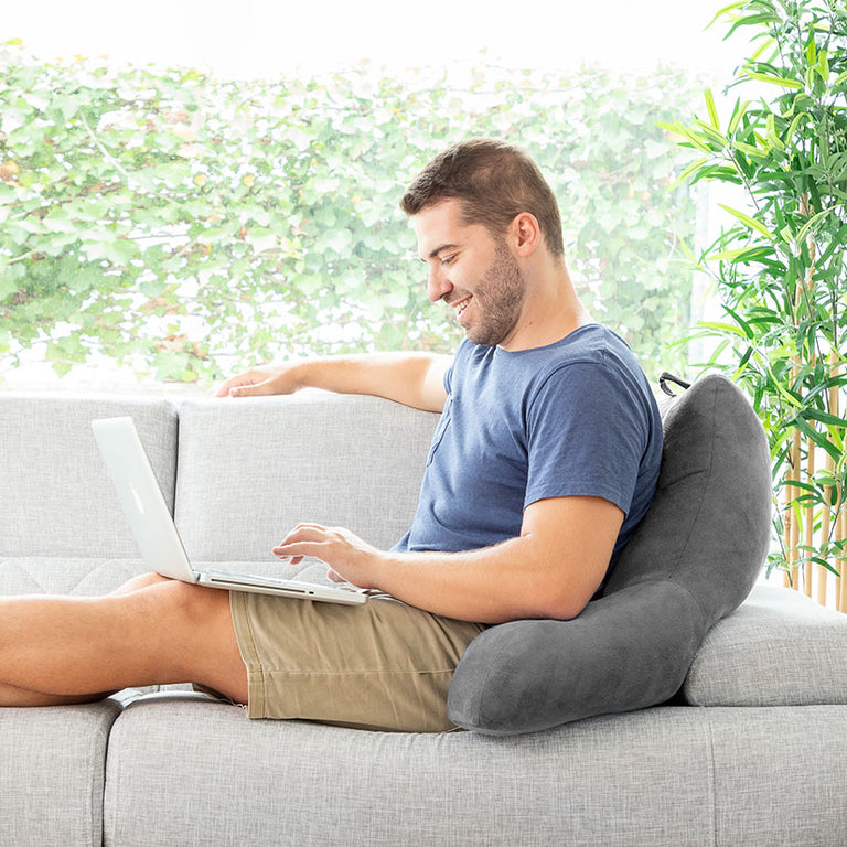 Hombre relajado en el sofá utilizando la almohada de lectura Huggilow mientras trabaja con un portátil