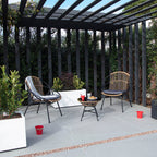 Sillones de exterior con estructura metálica negra y cojines grises situados bajo una pérgola de diseño.