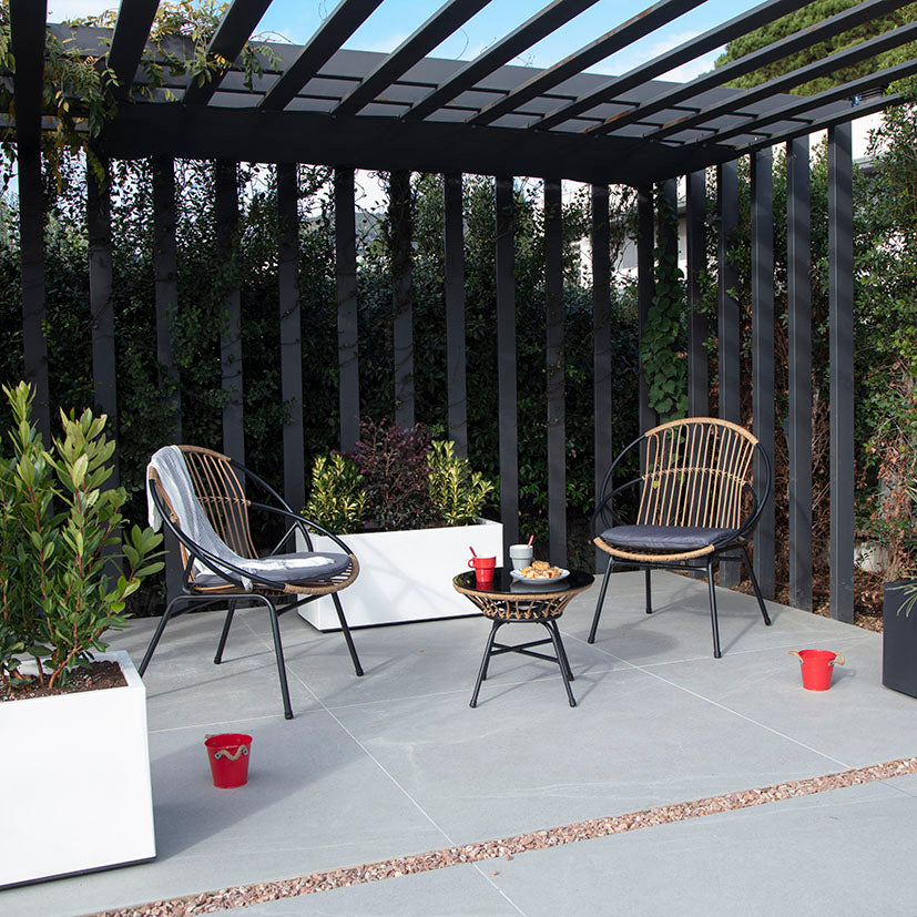 Sillones de exterior con estructura metálica negra y cojines grises situados bajo una pérgola de diseño.