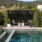 Zona de descanso exterior con conjunto Bistro de ratán junto a una piscina moderna y jardín perimetral.