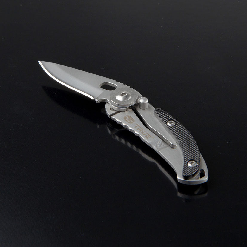 Navaja TRUE SkeletonKnife sobre superficie oscura resaltando su clip de bolsillo y acabados metálicos.
