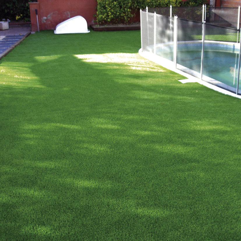 Instalación de césped artificial en zona de jardín con piscina y valla