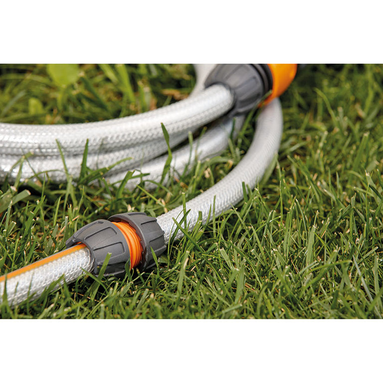 Conector reparador LISTA uniendo dos tramos de manguera de riego sobre césped de jardín