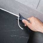 Rascador Wolfcraft de PRFV eliminando restos de silicona vieja entre azulejos de forma precisa.