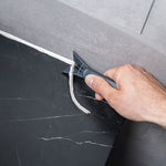 Rascador Wolfcraft de PRFV eliminando restos de silicona vieja entre azulejos de forma precisa.