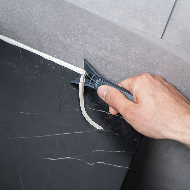 Rascador Wolfcraft de PRFV eliminando restos de silicona vieja entre azulejos de forma precisa.