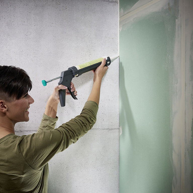 Usuario sellando esquina de pared de hormigón con pistola de cartuchos Wolfcraft MG 100.