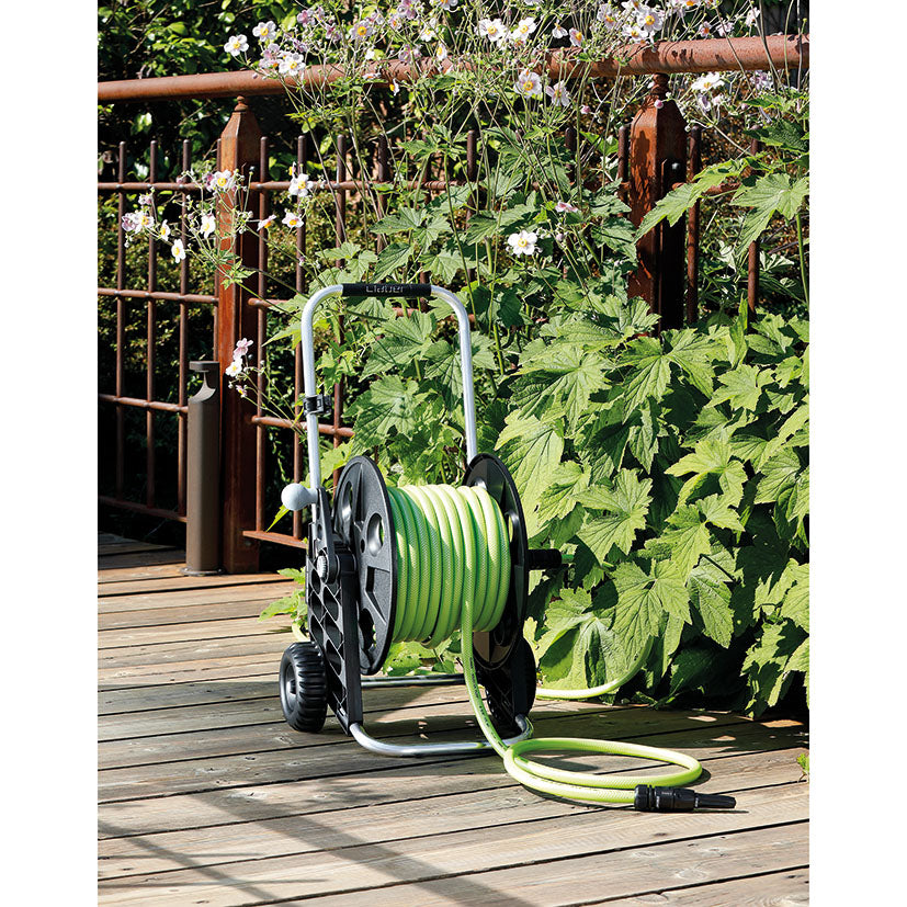Carro de riego Claber Genius en uso sobre suelo de madera en jardín, mostrando su portabilidad y diseño ergonómico.