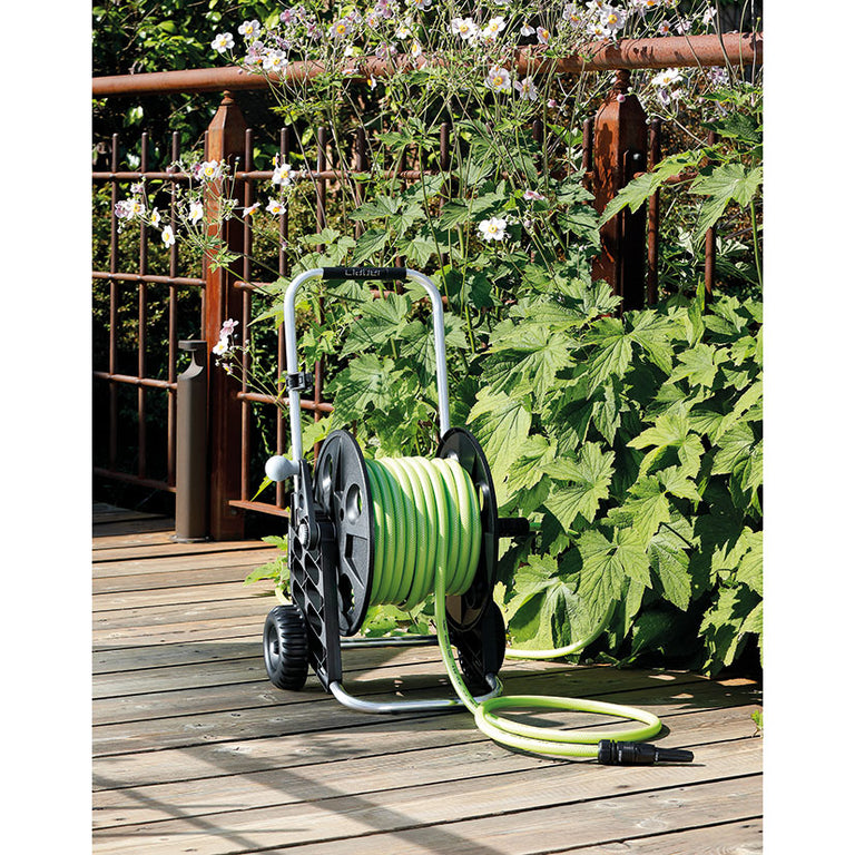 Carro de riego Claber Genius en uso sobre suelo de madera en jardín, mostrando su portabilidad y diseño ergonómico.