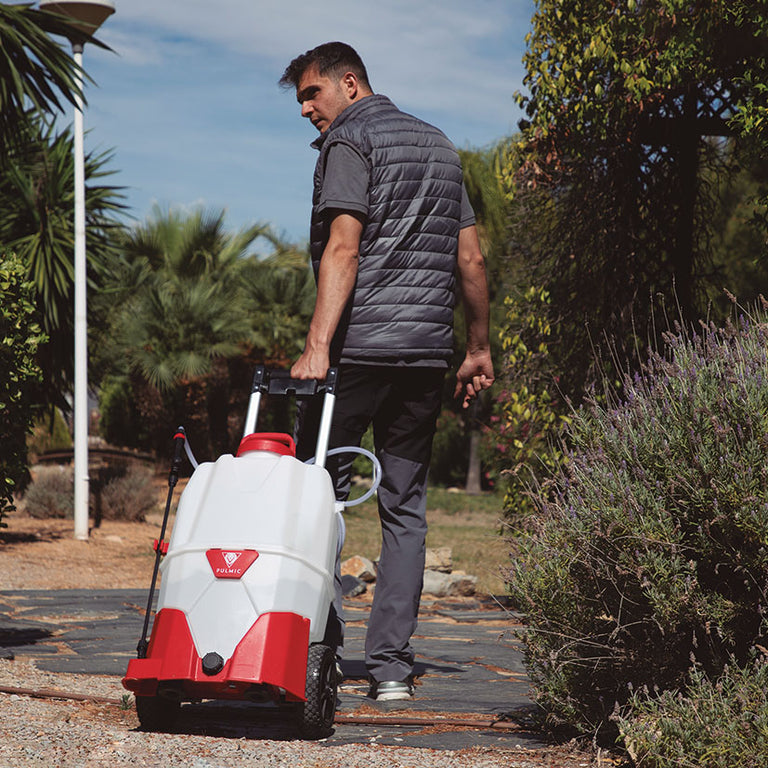 Usuario transportando el pulverizador a batería Pulmic Pegasus 35 mediante su asa ergonómica en un entorno de jardín.