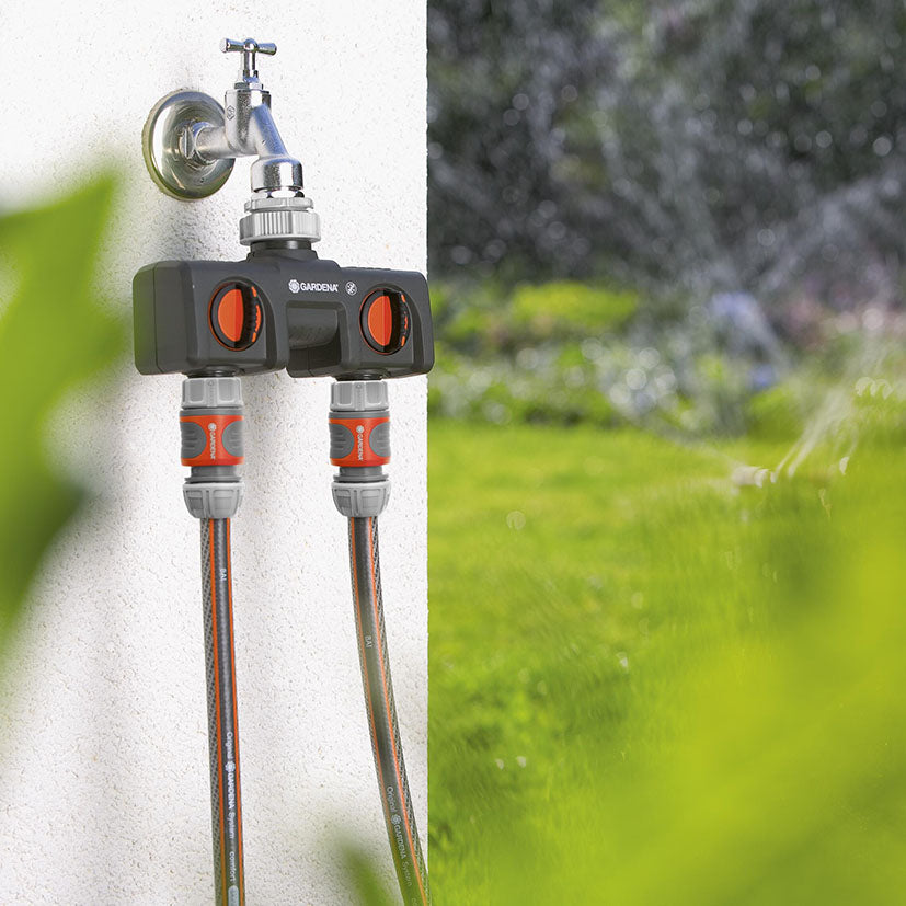Uso del distribuidor de 2 vías Gardena conectando dos mangueras de riego simultáneamente en un jardín.