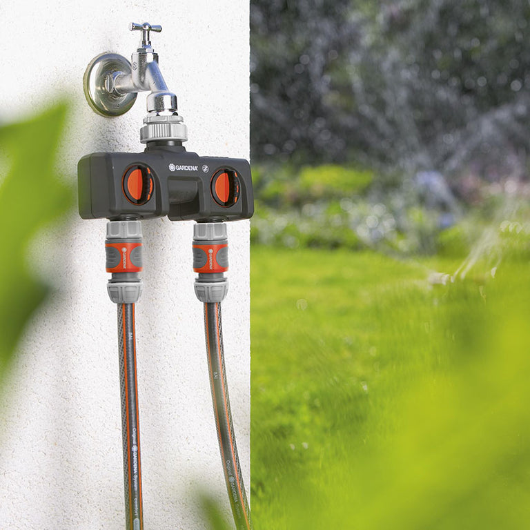 Uso del distribuidor de 2 vías Gardena conectando dos mangueras de riego simultáneamente en un jardín.