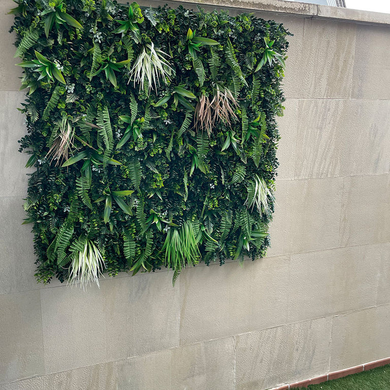 Jardín vertical artificial modelo Otoño de 100x100 cm instalado en una pared exterior de piedra clara.