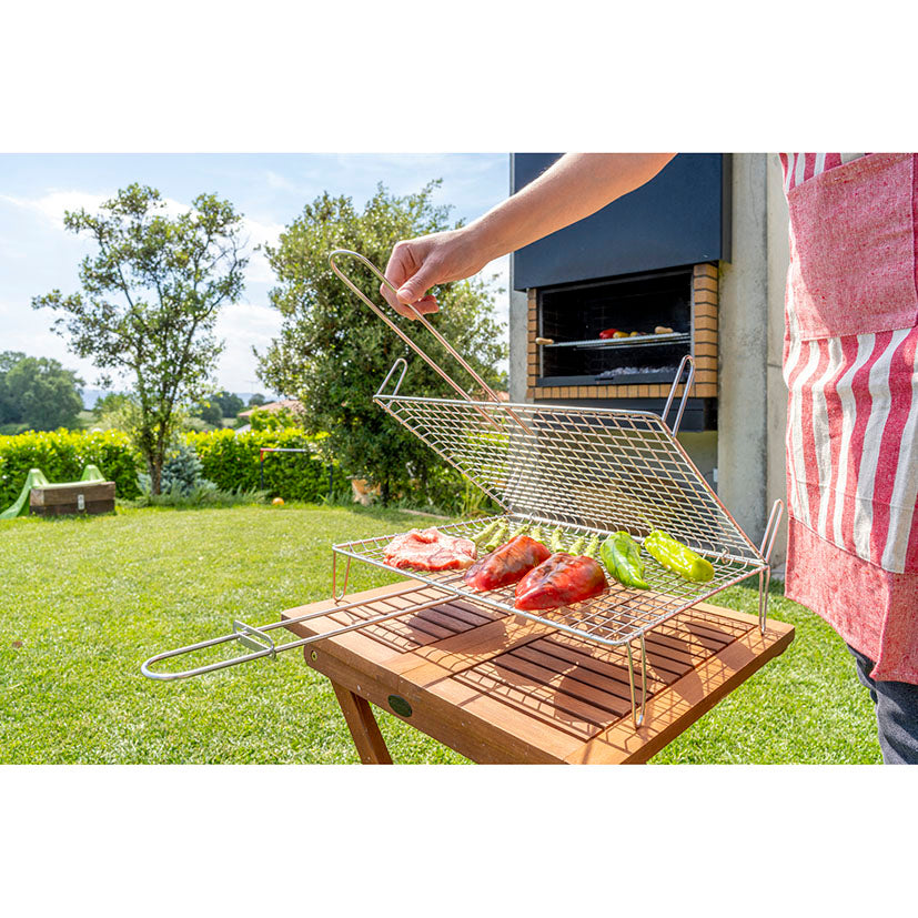 Uso de parrilla abombada Sauvic con carne y verduras sobre una mesa de madera en exterior.