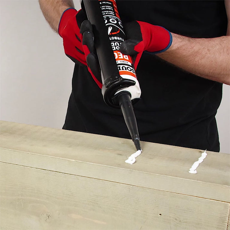 Aplicación de cordones de adhesivo blanco Turbotack con pistola de silicona sobre superficie de madera.