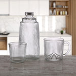 Botella y vaso de cristal Versa en ambiente de cocina moderna junto a una taza de café