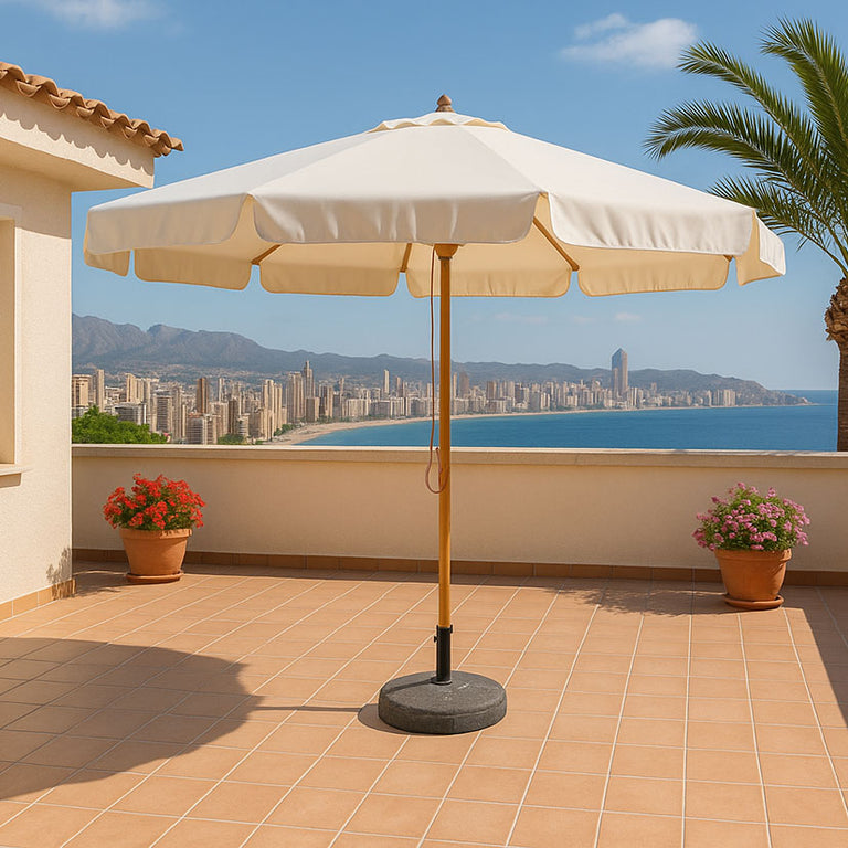 Sombrilla de jardín Deluxe 300 cm con sistema de polea y lona color crudo en terraza frente al mar.