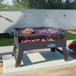 Barbacoa portátil Aventure C104 en uso sobre mesa exterior cocinando carne y verduras a la brasa.