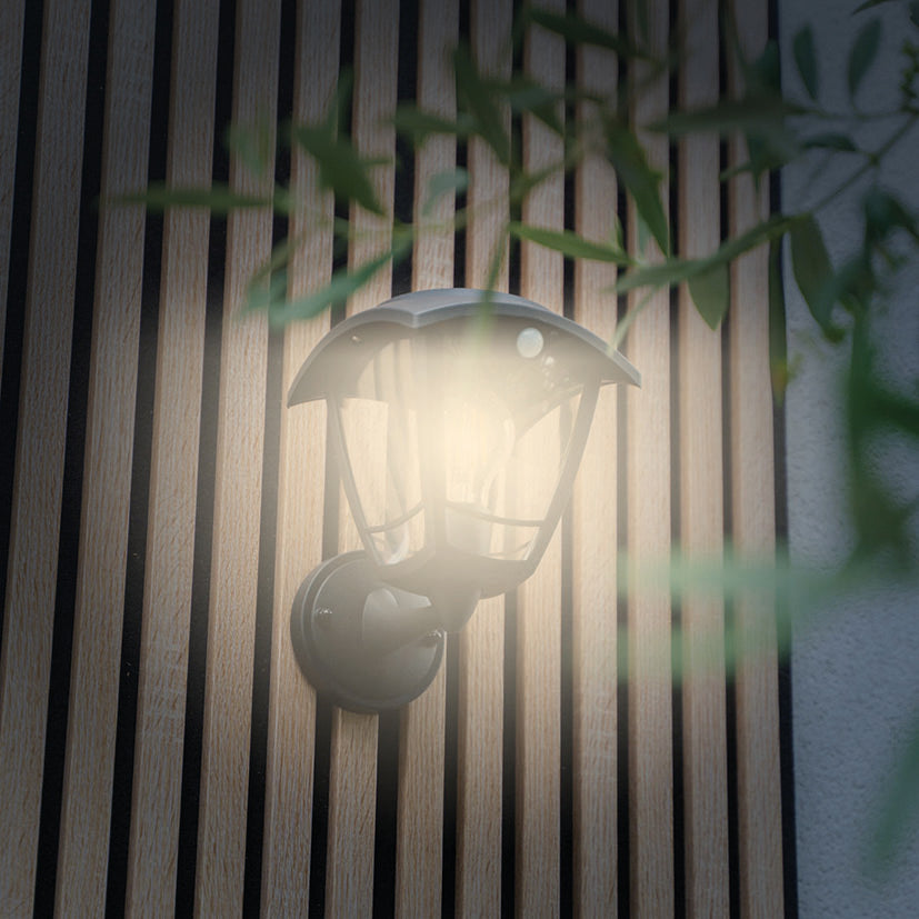 Detalle de aplique solar de pared con luz cálida encendida sobre revestimiento de madera exterior.
