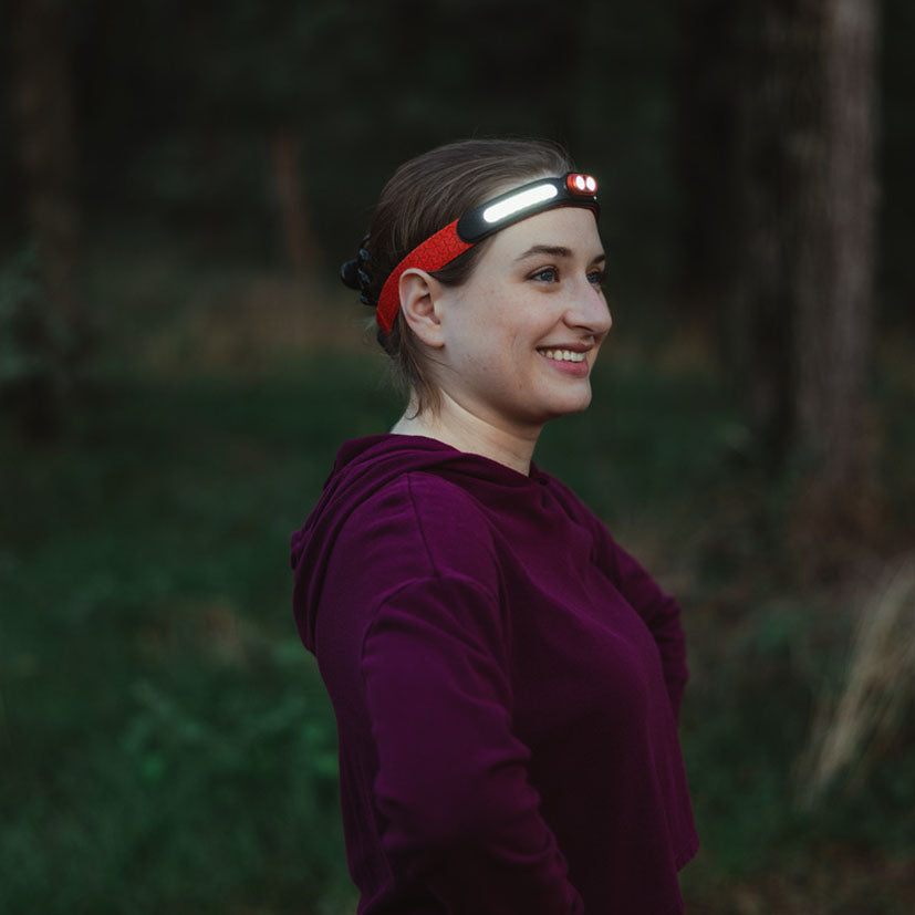 Mujer sonriente equipada con el frontal NEBO Curvbeam 600 Flex para actividades al aire libre.