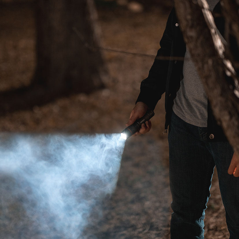 Uso nocturno de la linterna NEBO Davinci 1000 proyectando un haz de luz potente en el bosque.