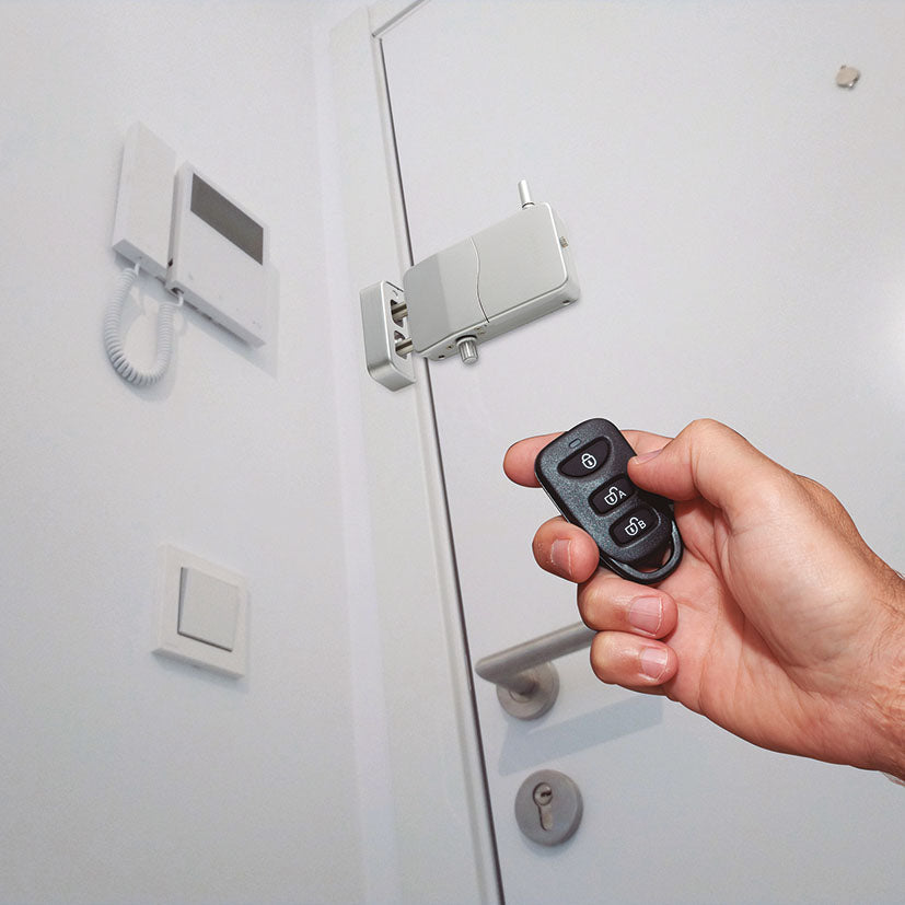 Mano accionando el mando a distancia de una cerradura invisible Arregui instalada en el interior de una puerta blanca moderna junto a un telefonillo.