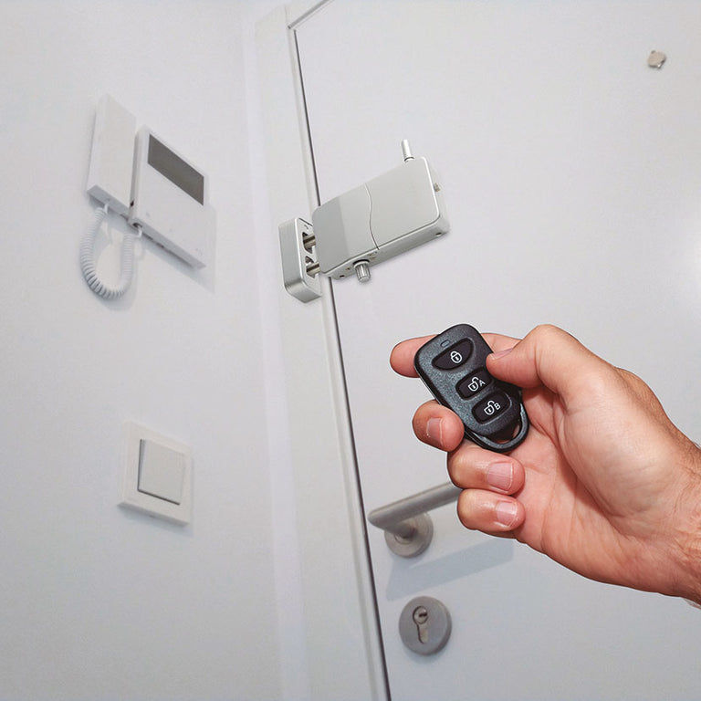 Mano accionando el mando a distancia de una cerradura invisible Arregui instalada en el interior de una puerta blanca moderna junto a un telefonillo.