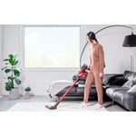 Mujer utilizando la aspiradora escoba Einhell TE-SV 18/270 en un salón moderno para limpiar una alfombra blanca, destacando su ergonomía y diseño sin cables.