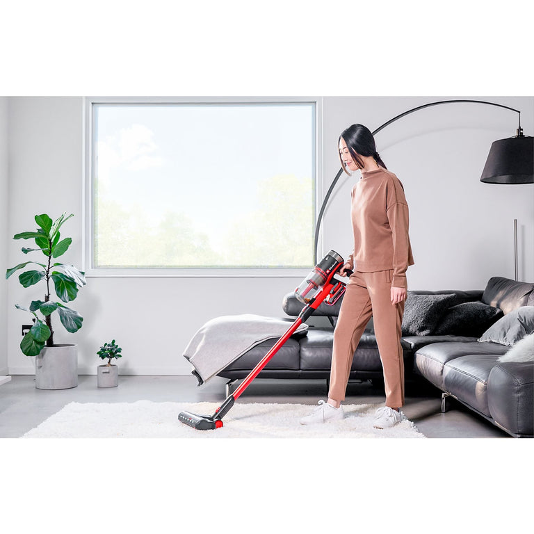 Mujer utilizando la aspiradora escoba Einhell TE-SV 18/270 en un salón moderno para limpiar una alfombra blanca, destacando su ergonomía y diseño sin cables.